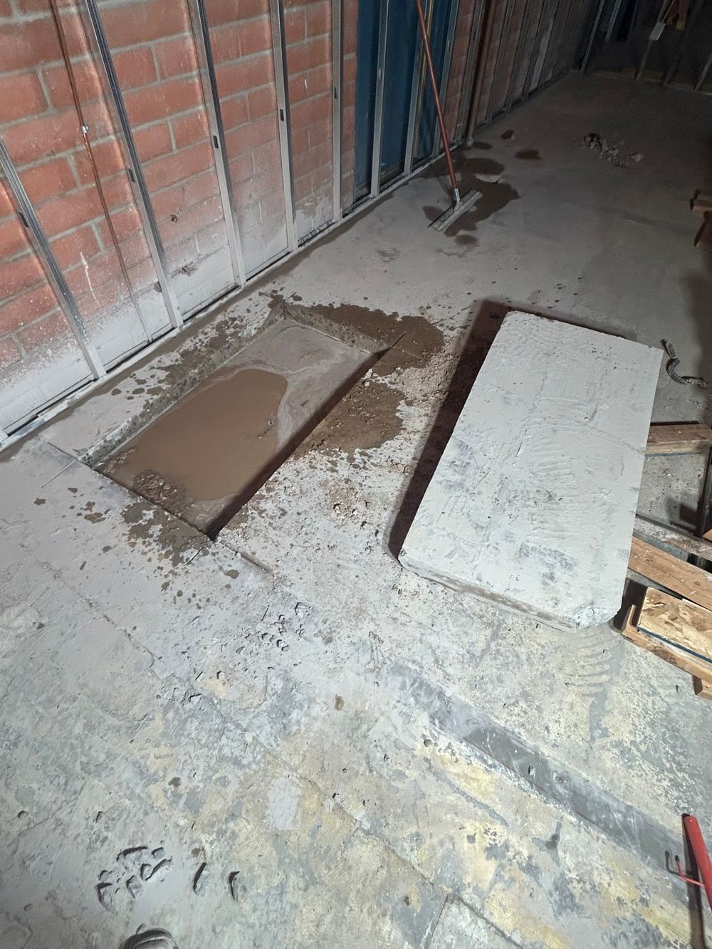 Saw-cut section of an interior concrete slab removed next to a brick wall
