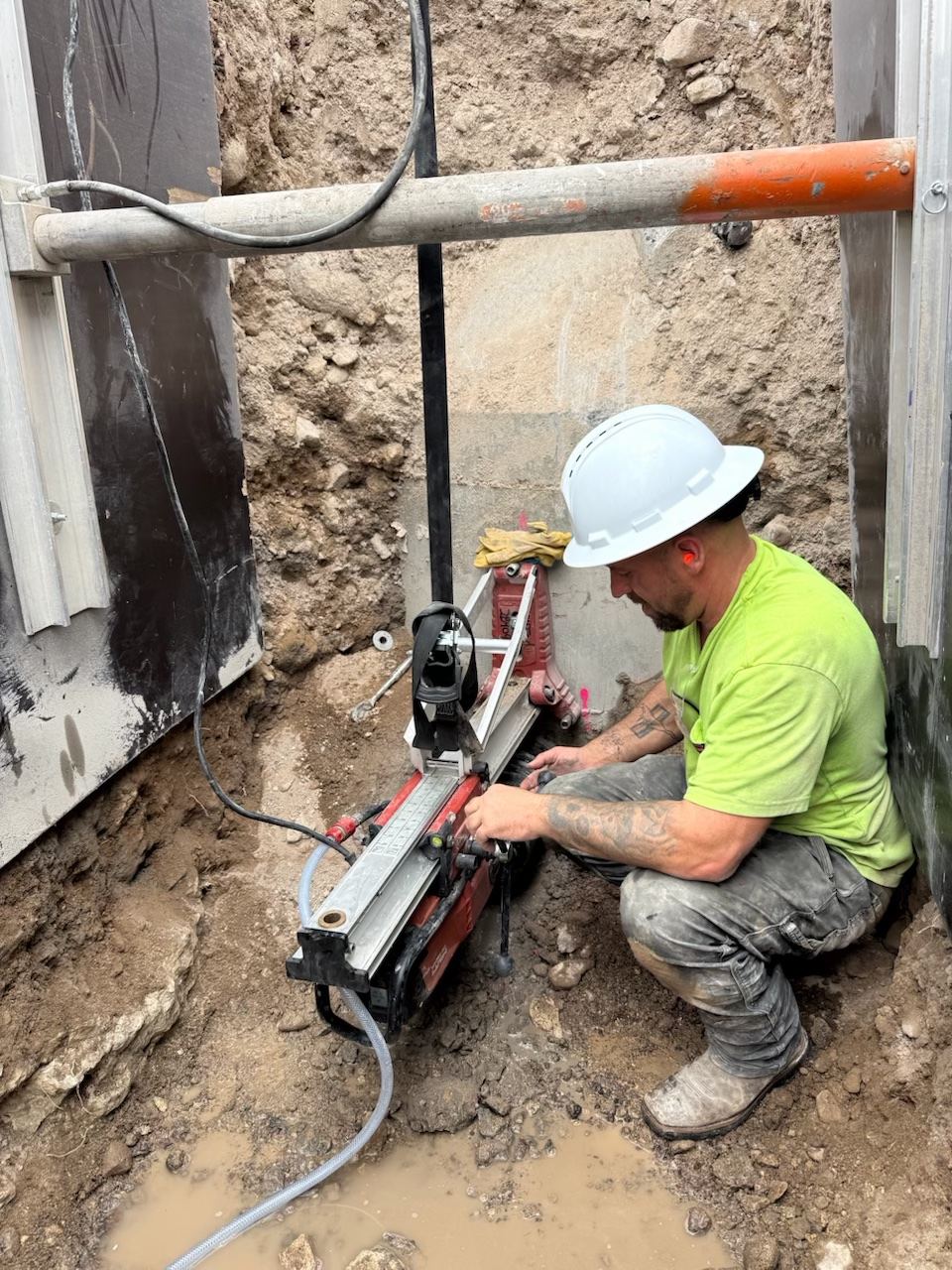 Desert Edge operator core drilling a pipe penetration into a concrete manhole in a shored trench