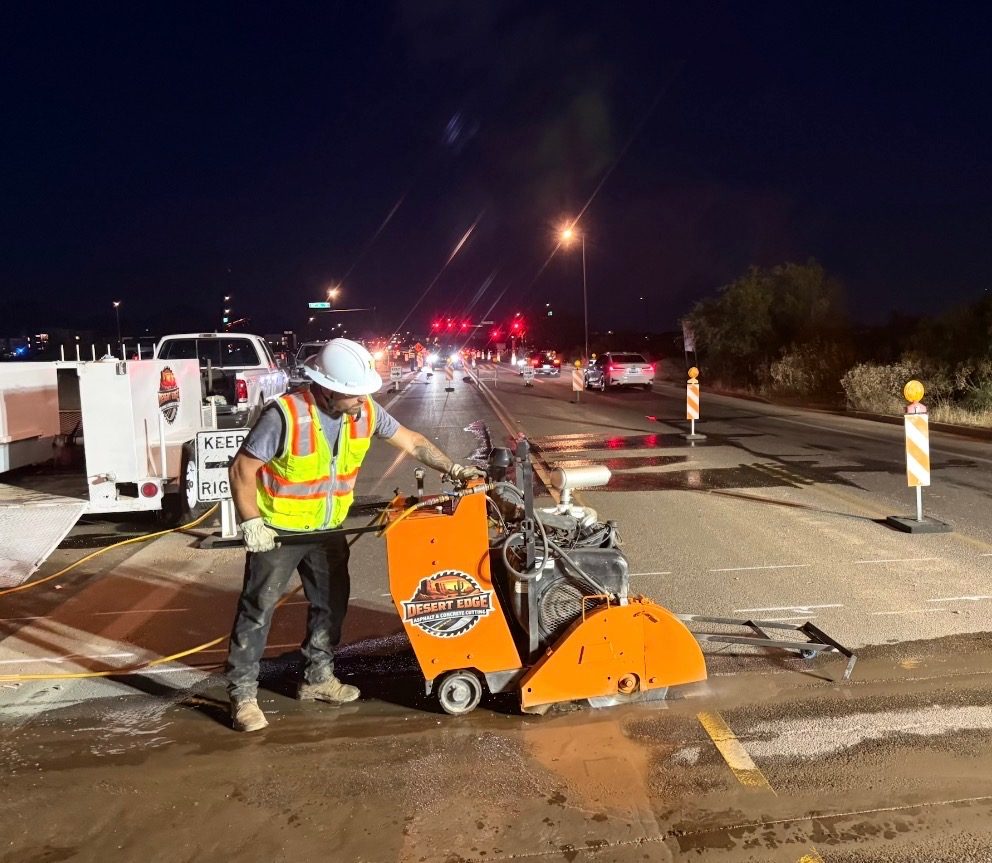 Desert Edge operator running a walk-behind saw on a roadway at night with traffic control